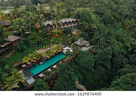 Aerial view of luxury hotel with straw roof villas and pools in tropical jungle and palm trees. Luxurious villa, pavilion in forest, Ubud, Bali. Royalty-Free Stock Photo #1629876400