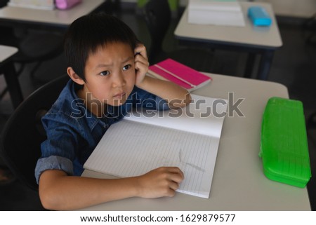 Thoughtful schoolboy looking away in classroom of elementary school