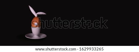 Easter bunny egg with cotton tail and ears on dark background with copyspace. Banner of moody minimalistic decoration concept. Stock photo.