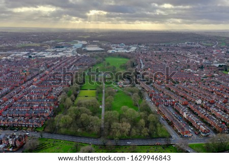 Aerial photo of the village of Beeston in Leeds West Yorkshire showing a typical British park along side rows of terrace houses, roads and streets, taken in the winter time on a wet cold day.