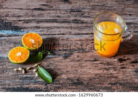 A glass of orange juice on a vintage wooden table, complemented by slices of fresh local oranges and their leaves. In Indonesia this drink is called jus jeruk.