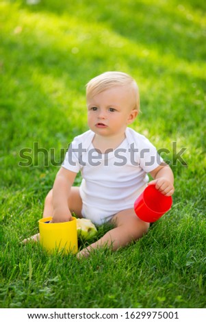 baby in a white bodysuit sitting on a green lawn playing with toys, space for text