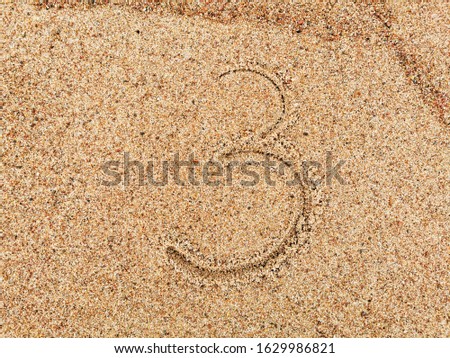 The inscription of handwritten number 3 on wet beach sand. 