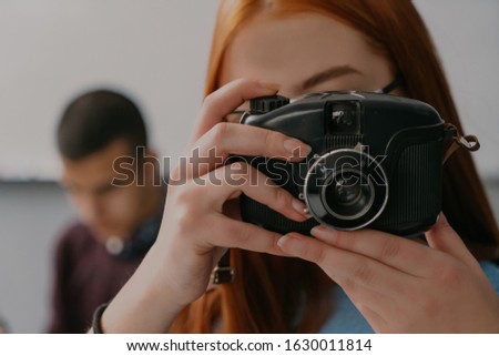 Little woman with glasses sitting on table and making photo on old camera