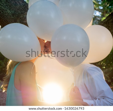 A kissing couple covered with white balloons in a garden under the sunlight