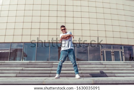 happy man smiles, young guy dancer, in summer in city, dancing street dance, modern youth style. Fashion and fitness sport. Free space for copy text. Step cloud background