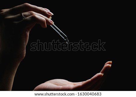 female with beautiful nails hold pipette over another hand, isolated on black background