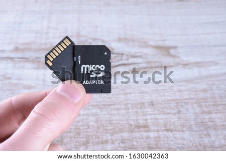 Hand holds flash drive, memory card adapter on wooden background. and close up