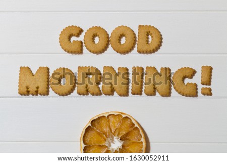 White wooden table with writing made with good morning cookies with orange wedge as sun rising to start a happy and positive day