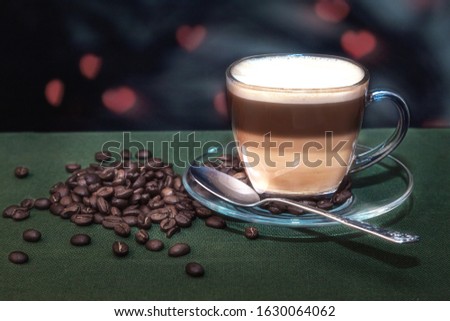 A Cup of coffee with milk on the table with a green cloth on a dark blurred background. Coffee beans are scattered on the table. Close up.