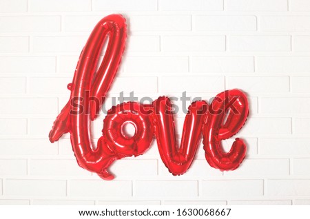 Foil red ball in the shape of the word love of red on a white brick wall on Valentine's Day holiday.