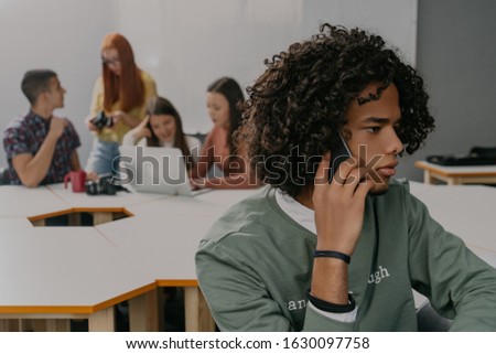 African man using phone, talking with friends, in background young people working on laptop and making designer for web