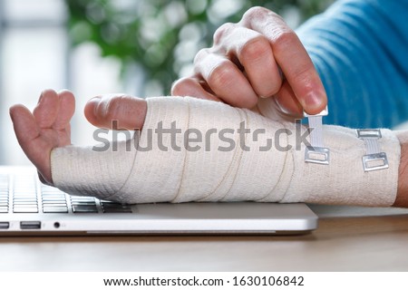 Close up of man arms wrapping his painful wrist with Flexible elastic supportive orthopedic bandage caused by prolonged work on laptop. Carpal tunnel syndrome, arthritis, arm sprain concept. 