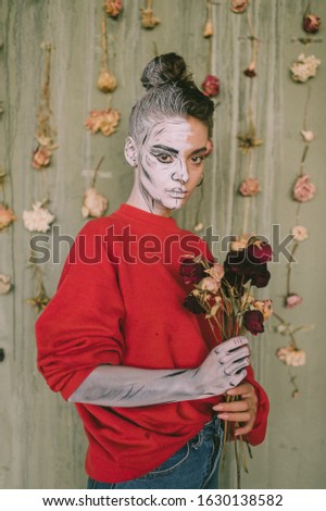 Young girl with creative body art standing against decorative wallpaper with dried flowers.