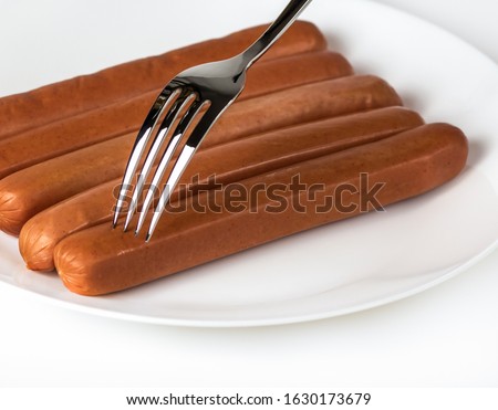 French uncooked hot dog sausages and a fork puncturing them on white plate and white background.