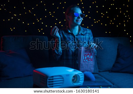 Home entertainment, watching movies and movies, a girl in 3D glasses with popcorn on a sofa at home watching movies through a projector