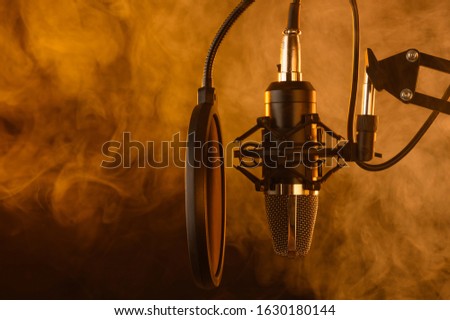 Close up studio condenser microphone on stand and anti-vibration mount. Live recording with colored lights background. Side view.Yellow light, smoke.Karaoke