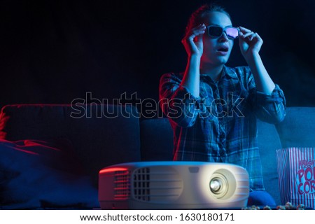 Cinema and movies in 3D. A girl looks in 3D glasses with a projector and popcorn