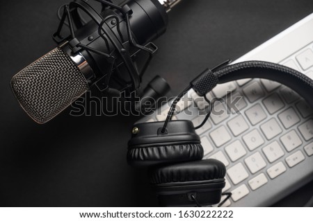Microphone for podcasts and studio headphones on a PC keyboard on a black background, horizontal frame
