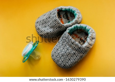 soft slippers made of cotton and ecological fabrics for a very small newborn with blue pacifier on a bright even yellow background