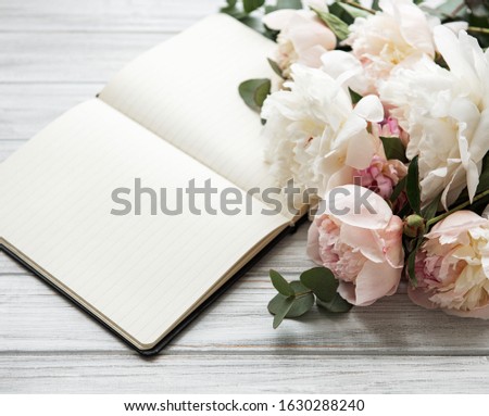 Flat lay blogger or freelancer workspace with a notebook, pink peonies on a white wooden  background