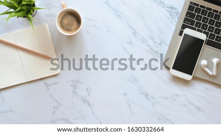 Marble office desk with Laptop, black blank screen smartphone, wireless earphone, pencil, notes and potted plant putting. Flat lay working equipment concept.