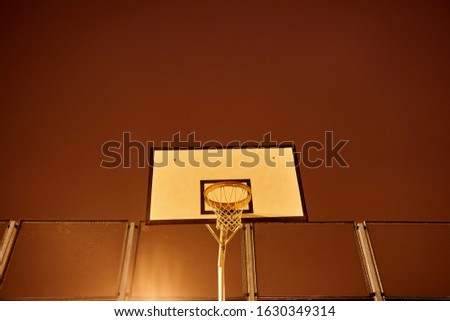 a ring and a shield for playing basketball on an open-air playground at an altitude in the dark in the evening against a background of orange foggy sky