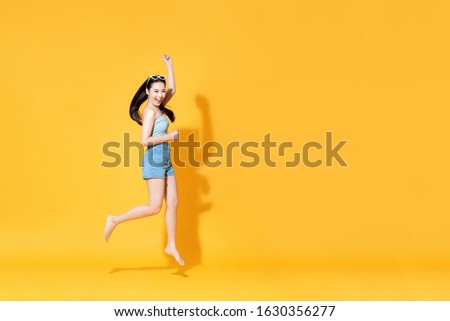 Energetic smiling beautiful Asian woman in summer outfit jumping isolated on yellow background Royalty-Free Stock Photo #1630356277