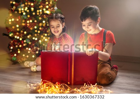 Two children are sitting near the New Year tree, looking at the book