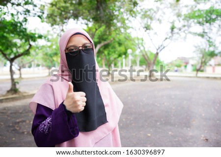 Portrait of pretty hijab women wearing niqab showing thumbs up or best gesture outdoor.