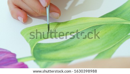 Painter holding a paintbrush in his hand. Watercolor drawing - flowers - and artistic equipment on desk. Top view. Painter drawing at working place.