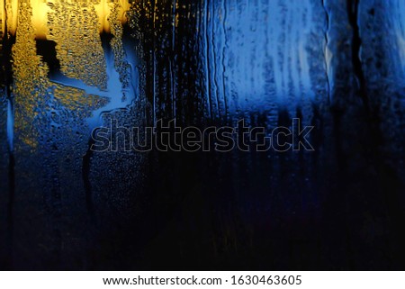 Blurred many droplets on a glass room with yellow blue light bulb glowing in the dark night and black color background 