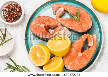 Raw Salmon steak in blue plate with ingredients for cooking. Top view on white stone table.