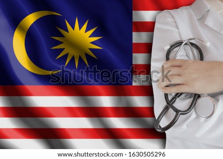 The concept of the level of medicine in the country, the salary of a doctor, the incidence rate in the country. Doctor holds a stethoscope on the background of the flag of Malaysia