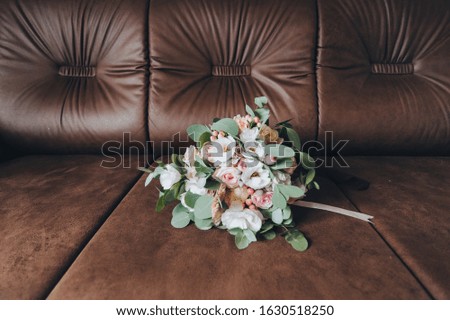 A wedding bouquet of roses and eustomas lies on a brown leather sofa close-up. Photography, concept.