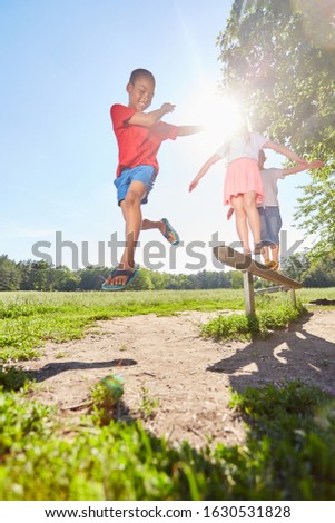 Children jump from a balancing bar in the summer in the park
