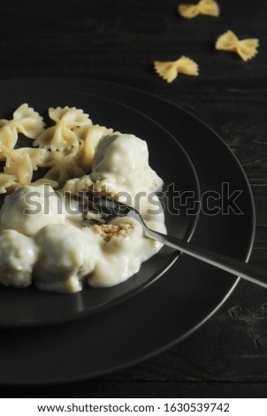 Meatballs in a creamy sauce with bow-shaped pasta on a black plate. Copy space. Dark photo.