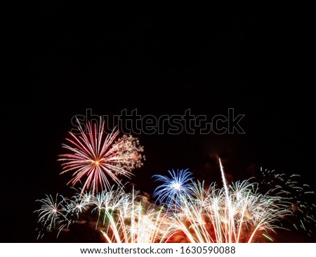 Red starburst, blue starburst over gold and white fireworks with a black background
