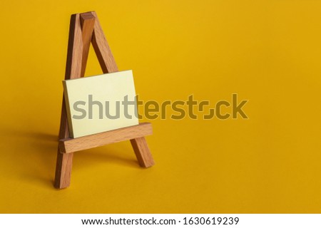 Yellow sticker with empty place for an inscription. Mini easel with a sticker on a yellow background.