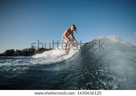 Young muscular wakesurfer conquers a high wave on a board on a sunny day