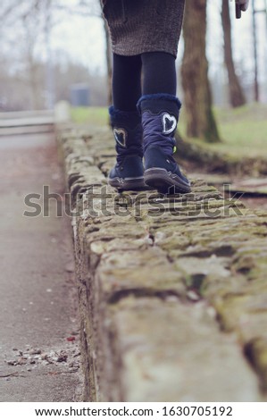 A girl walking on a mossy, damp wall during boring winter holidays devoid of snow. Sad winter without snow, boring and gloomy January morning.