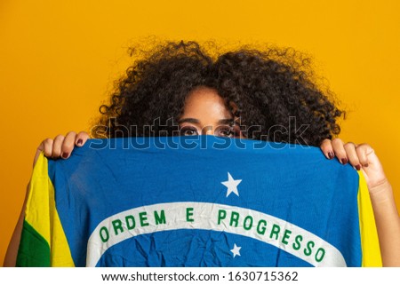 Misterious black woman fan holding a Brazilian flag in your face. Brazil colors in background, green, blue and yellow. Elections, soccer or politics.