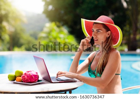 Woman with laptop at swimming pool. Remote work and global nomad concept. Young female freelancer in tropical resort. Conference call and freelance job. Girl in bikini with computer and mobile phone.