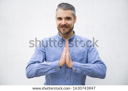 Handsome smiling young man praying. Handsome young man with hands together in praying gesture. Hope and please concept