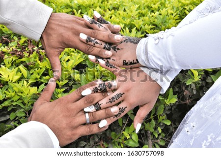 Four hands: a bride with a pattern of black henna on her fingers in oriental style and a male groom on a background of green leaves. .Not a tattoo. Newlyweds, love, wedding, greeting card, invitation,