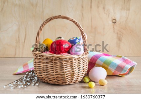 Easter holiday still life. Wicker basket with different eggs, checkered napkin and bouquet of willow twigs on wooden background