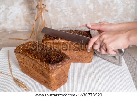 freshly baked sliced bread on rustic wooden table. Women's hands take the bread in a linen napkin. Knife Bread