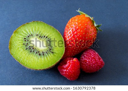 Kiwi, strawberry and two raspberries in a close-up against gray background.