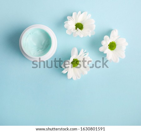 
Natural cream in a jar with a flower on a blue background