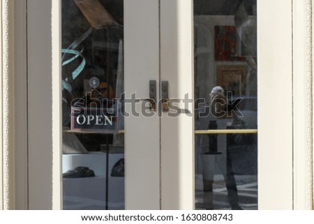Anonymous street photographer reflected in shop window. Open sign on door. Colorful blurred shop interior.